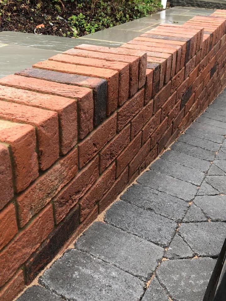 A low brick garden wall with a soldier-course top, meeting new charcoal block paving.