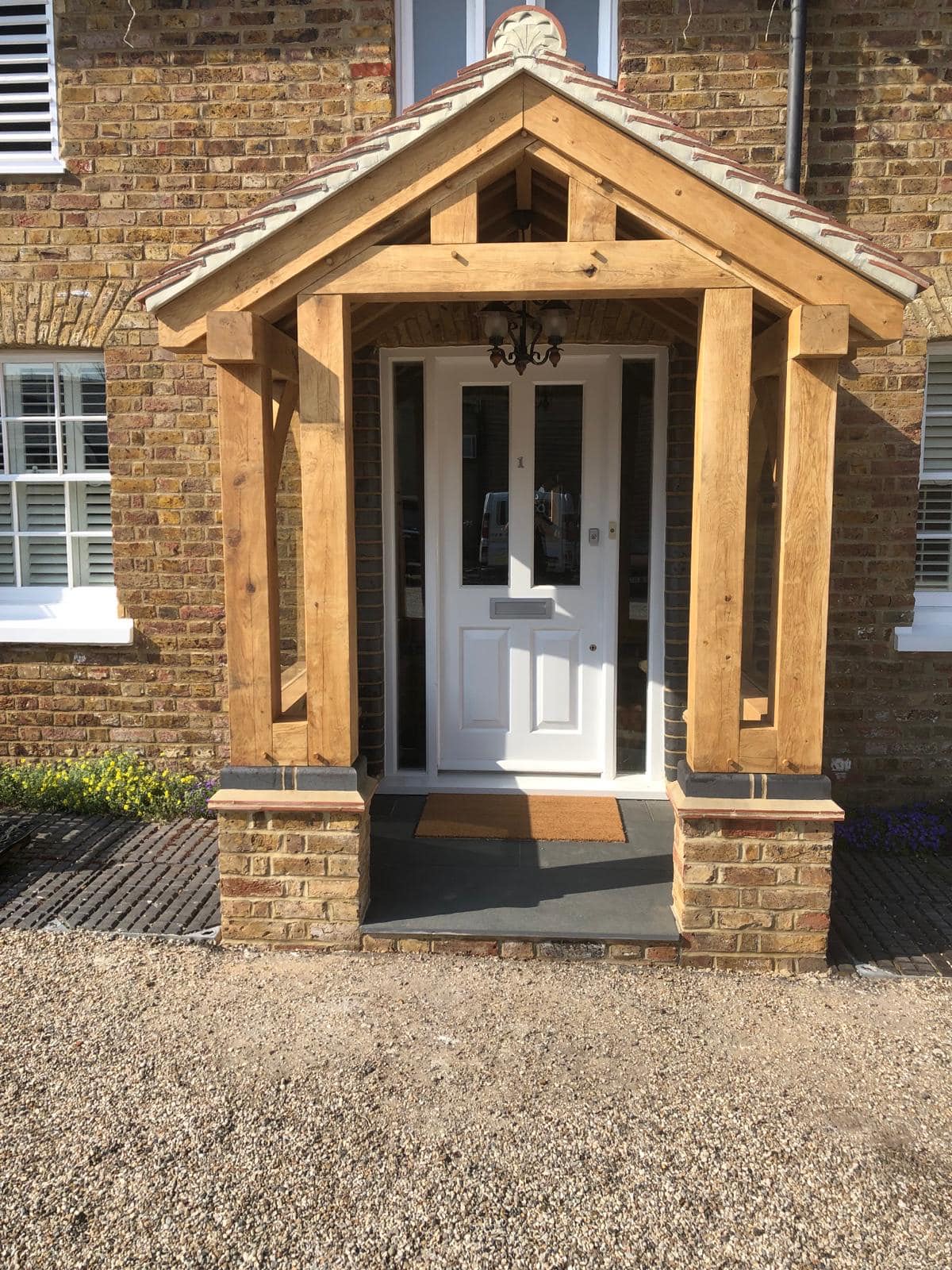 A green-oak porch canopy on brick piers, framing a period front door.